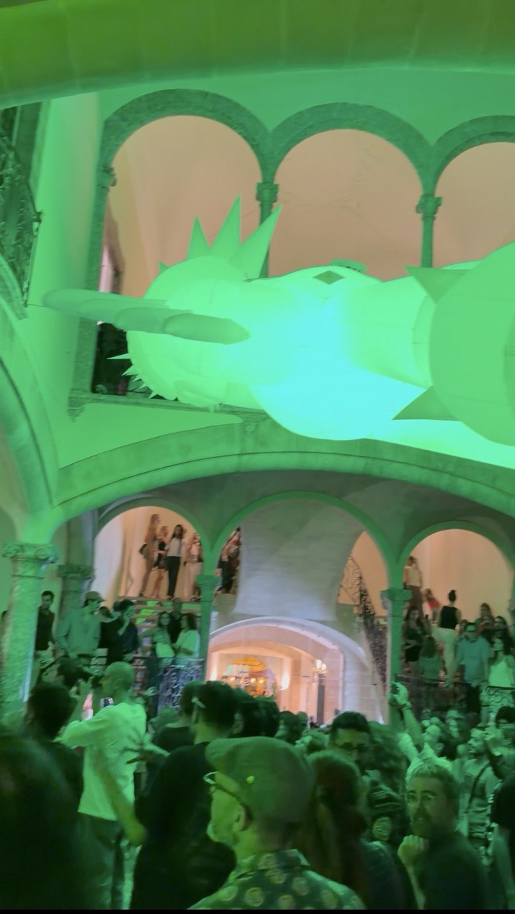 Green-lit historic courtyard with a glowing floating sculpture and crowds during Nit de l'Art