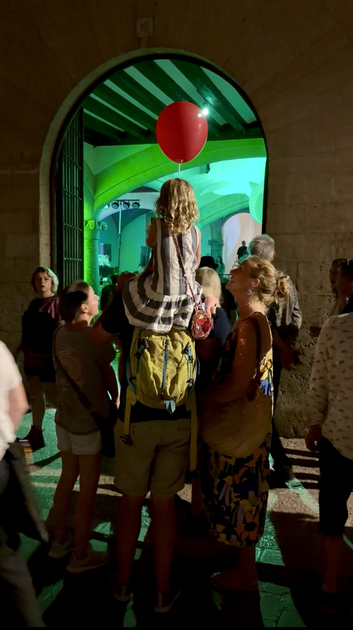 Gallery-goers by a green-lit doorway with a red balloon on Nit de l'Art