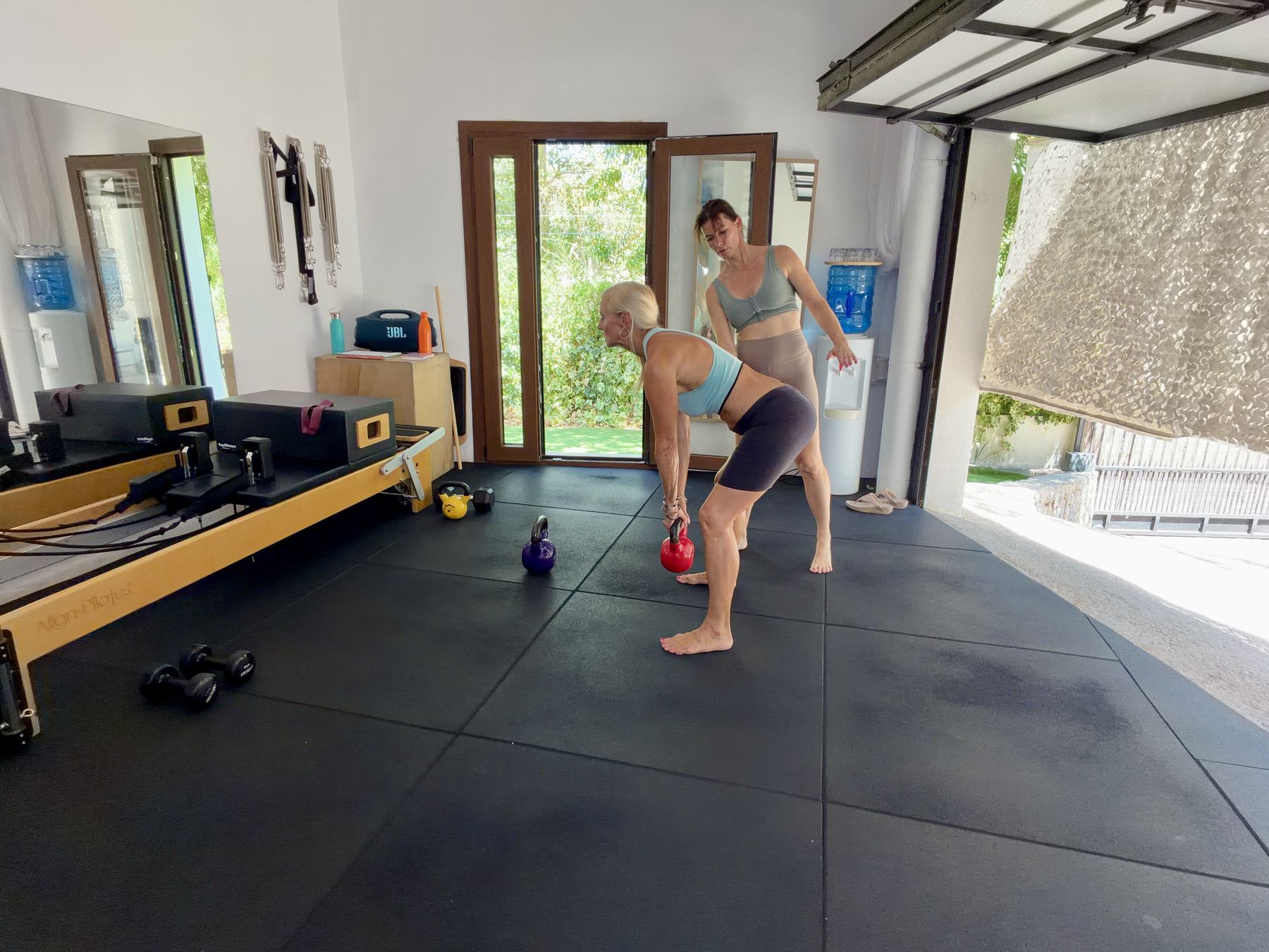 Amanda J Butler practising a kettlebell deadlift with personal trainer Kate Sotelo coaching her form in a garden training studio in Mallorca