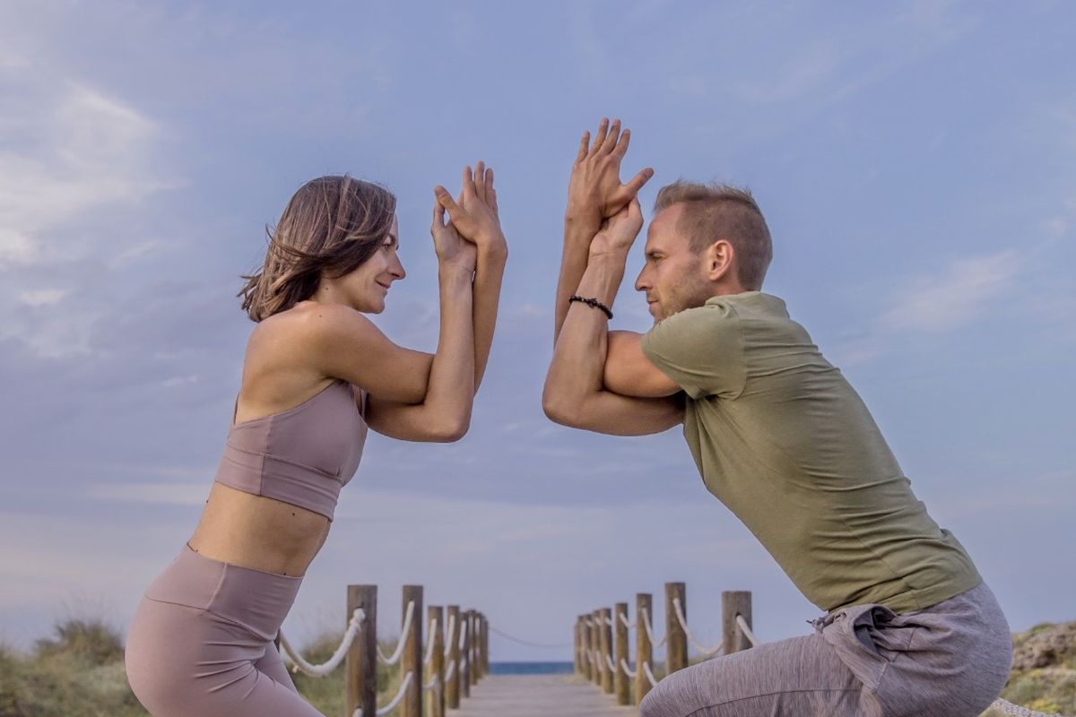 Yoga teachers Lilla and Peter of Our Yoga Mind in eagle arms on a beach boardwalk, Harmonising Yin and Yang retreat day, Mallorca