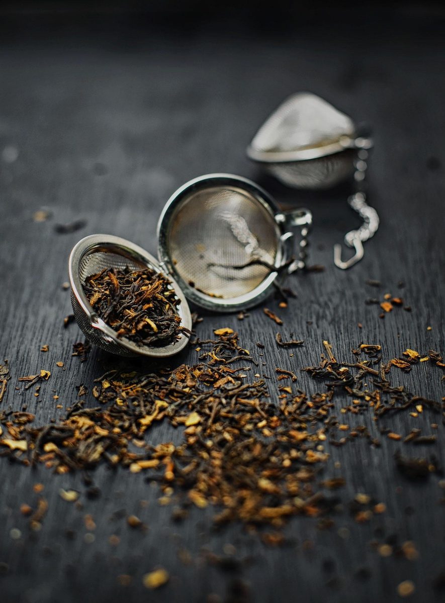 Loose-leaf black tea spilling from an open stainless-steel tea infuser ball