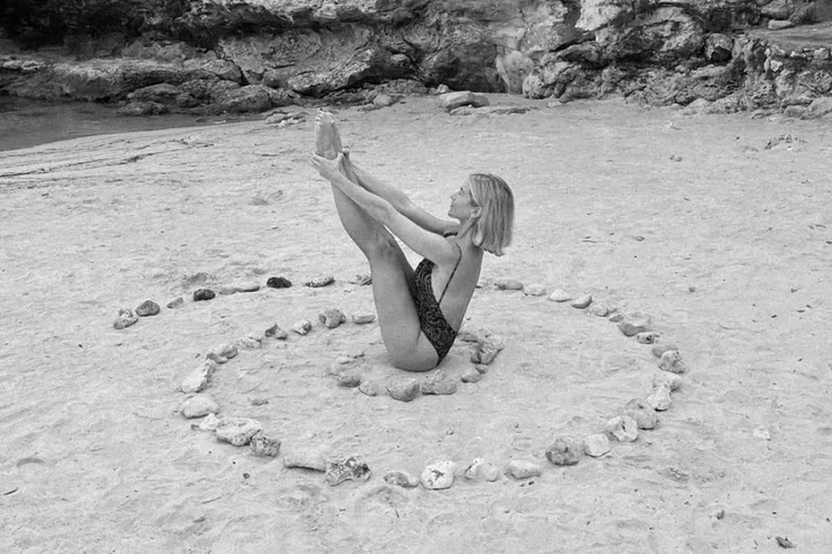 Yoga teacher in boat pose inside a stone circle on a Mallorca beach, yoga retreat at Osa Major