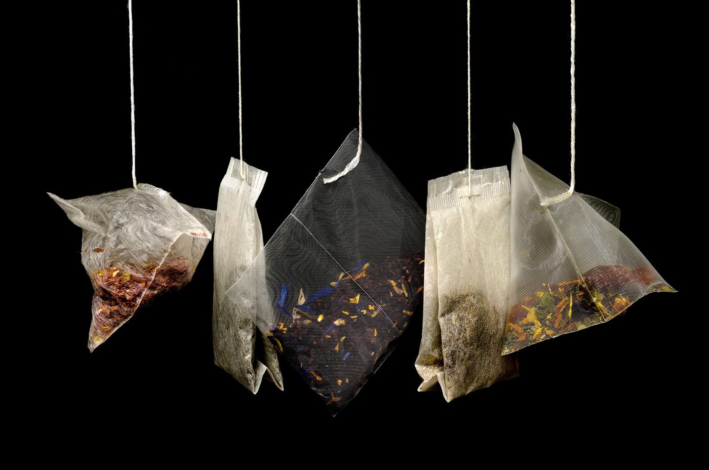 Five tea bags hanging on strings, including shiny pyramid mesh bags and flat paper bags