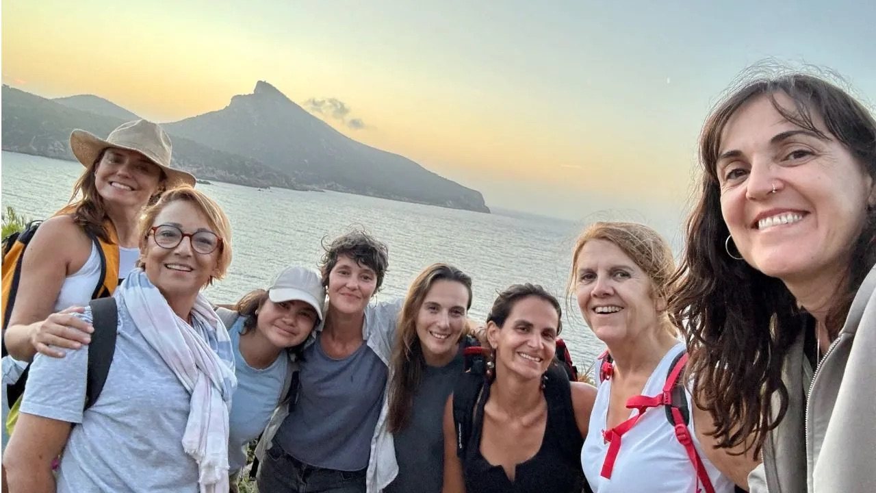 Women from the Sacar Pecho documentary smiling at sunset on the GR221 trail, with the island of Sa Dragonera behind, Mallorca