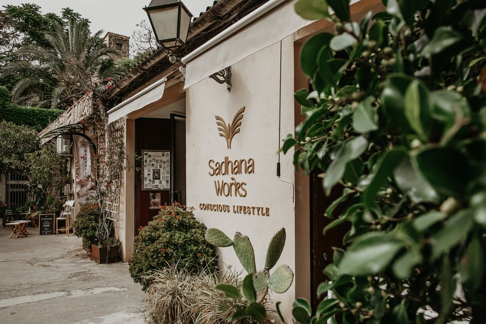 Entrance to Sadhana Works in Palma's Borne district, framed by greenery and a cactus garden