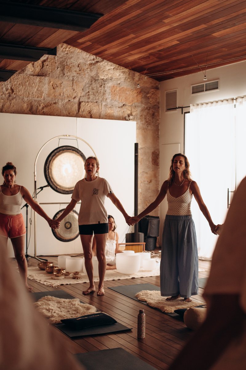 Women holding hands in a circle beside a gong at Sadhana Works in Palma